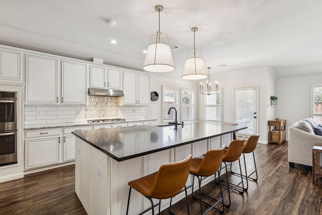 7716 Glenoaks Dr, Frisco, TX 75034 - kitchen featuring under cabinet range hood, stainless steel appliances, tasteful backsplash, dark wood-style floors, and ornamental molding