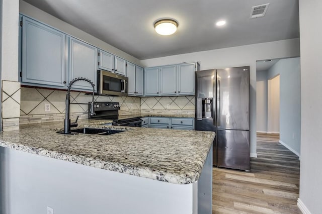 1004 Brae Loch Dr, Dallas, TX 75217 - kitchen with stainless steel appliances, a peninsula, light wood-style flooring, backsplash, and light stone countertops