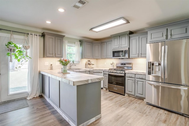 3025 Friendswood Dr, Arlington, TX 76013 - kitchen with appliances with stainless steel finishes, gray cabinetry, a peninsula, crown molding, and light wood-style flooring