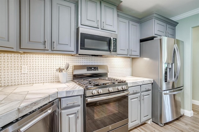 3025 Friendswood Dr, Arlington, TX 76013 - kitchen featuring stainless steel appliances, gray cabinets, ornamental molding, decorative backsplash, and tile countertops