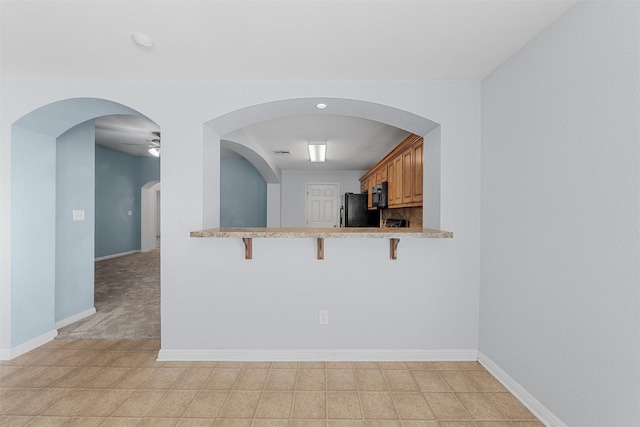708 Sapphire Blvd, Hewitt, TX 76643 - kitchen with freestanding refrigerator, a kitchen bar, light tile patterned floors, and brown cabinets