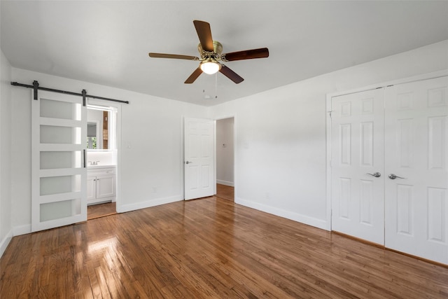 3501 Alta Vista Dr, Waco, TX 76706 - unfurnished bedroom with a barn door, a closet, wood finished floors, ensuite bathroom, and a ceiling fan