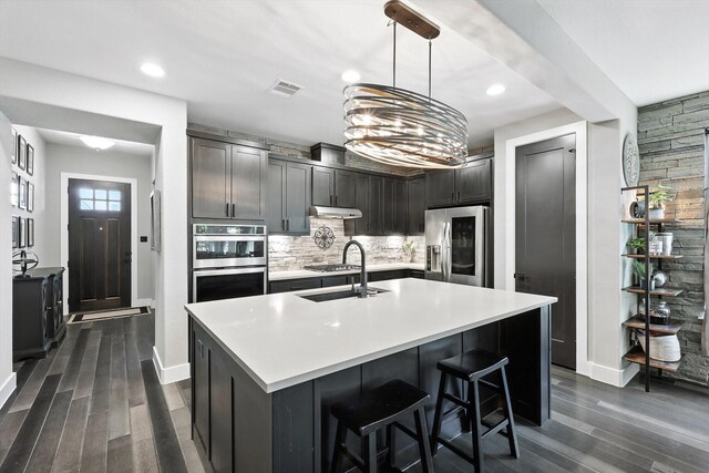 1521 Twistleaf Rd, Flower Mound, TX 76226 - kitchen featuring appliances with stainless steel finishes, dark wood-style floors, backsplash, light countertops, and a center island with sink