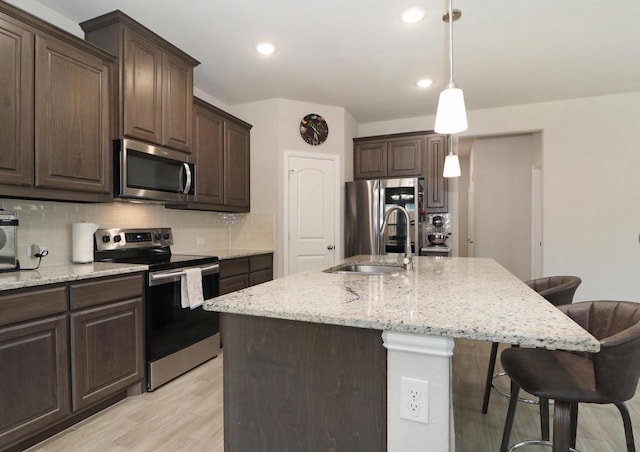 505 Reatta Dr, Justin, TX 76247 - kitchen featuring appliances with stainless steel finishes, a breakfast bar, backsplash, light wood-style flooring, and dark brown cabinetry