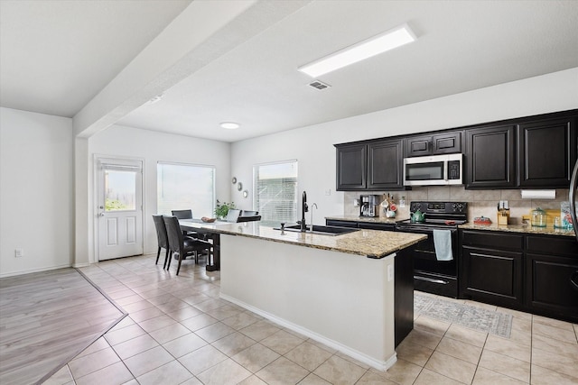 616 Cameron Way, Azle, TX 76020 - kitchen with stainless steel microwave, black / electric stove, light stone countertops, tasteful backsplash, and a kitchen island with sink