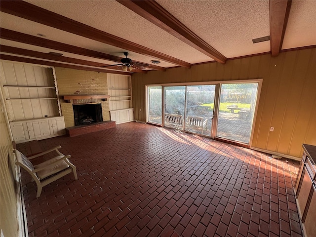 2928 Pine Ave, Waco, TX 76708 - unfurnished living room with beamed ceiling, a ceiling fan, a textured ceiling, wooden walls, and a brick fireplace