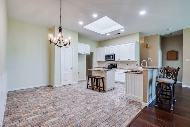 6051 W Fall Dr, Midlothian, TX 76065 - kitchen with appliances with stainless steel finishes, a breakfast bar area, a skylight, backsplash, and white cabinetry