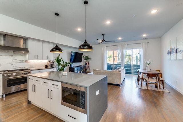 1901 N Carroll Ave Unit 104, Dallas, TX 75204 - kitchen featuring appliances with stainless steel finishes, a center island, decorative backsplash, wood finished floors, and a ceiling fan
