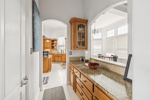 5210 Masters Ct, Midlothian, TX 76065 - kitchen featuring brown cabinets, arched walkways, glass insert cabinets, and light tile patterned floors