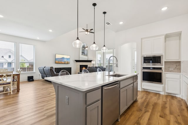 1814 Cypress Gap Trl, Mansfield, TX 76063 - kitchen featuring appliances with stainless steel finishes, gray cabinetry, open floor plan, light wood-style floors, and a warm lit fireplace