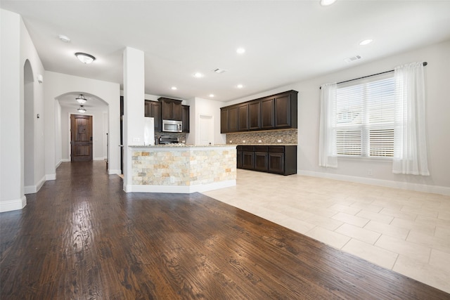 1020 Perennial Ln, Little Elm, TX 75068 - kitchen with stainless steel microwave, arched walkways, dark brown cabinets, backsplash, and white refrigerator