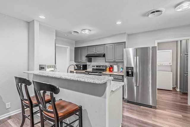 1007 College Ave, Glen Rose, TX 76043 - kitchen with stainless steel appliances, stacked washer / drying machine, under cabinet range hood, a breakfast bar, and wood finished floors