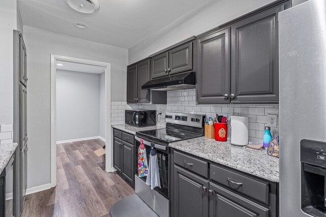 1007 College Ave, Glen Rose, TX 76043 - kitchen featuring appliances with stainless steel finishes, under cabinet range hood, dark wood finished floors, tasteful backsplash, and light stone counters