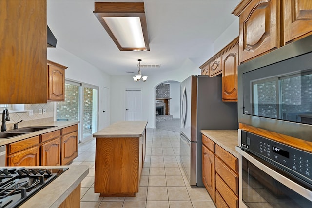 1645 Ashbourne Dr, Rockwall, TX 75087 - kitchen featuring appliances with stainless steel finishes, tasteful backsplash, a center island, light countertops, and a brick fireplace