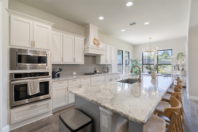 1253 Gray Fox Ln, Frisco, TX 75033 - kitchen featuring stainless steel appliances, a chandelier, white cabinetry, a center island with sink, and decorative backsplash