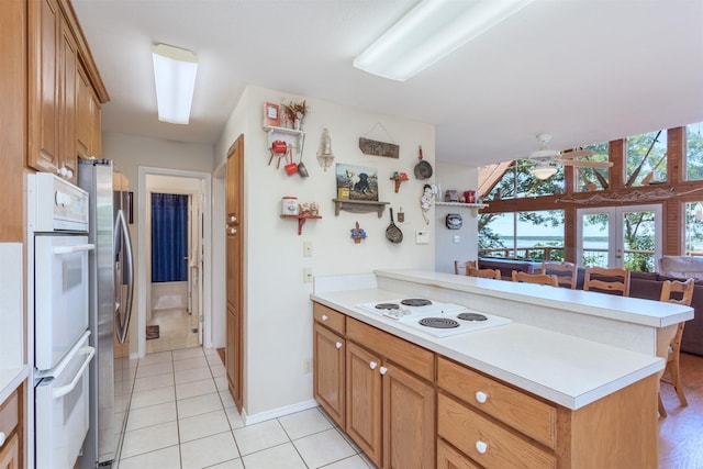 110 Waterview Ln, Pottsboro, TX 75076 - kitchen with white appliances, a peninsula, light countertops, light tile patterned flooring, and brown cabinets