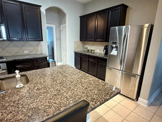 12713 Travers Trl, Fort Worth, TX 76244 - kitchen with stainless steel fridge, arched walkways, dark stone countertops, backsplash, and light tile patterned flooring