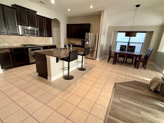 12713 Travers Trl, Fort Worth, TX 76244 - kitchen featuring appliances with stainless steel finishes, a kitchen breakfast bar, dark stone counters, arched walkways, and tasteful backsplash