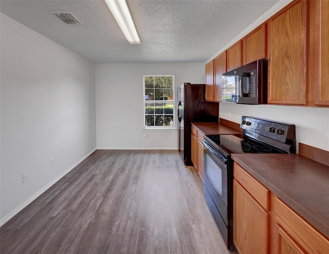 2428 Marimont Ln, Lancaster, TX 75134 - kitchen with black appliances, light wood-type flooring, a textured ceiling, dark countertops, and brown cabinetry