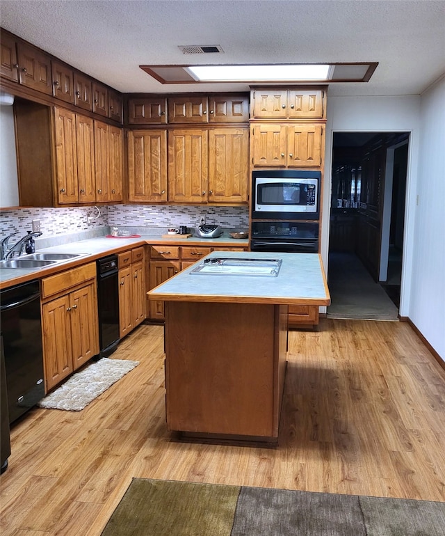 697 Highland Crest Dr, Hurst, TX 76054 - kitchen with black appliances, light countertops, light wood-style flooring, a center island, and tasteful backsplash
