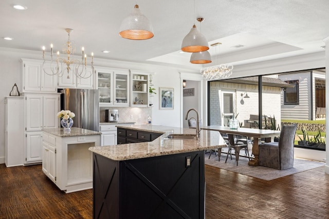 1212 Chandler Cir, Prosper, TX 75078 - kitchen with a center island with sink, freestanding refrigerator, a chandelier, glass insert cabinets, and white cabinetry