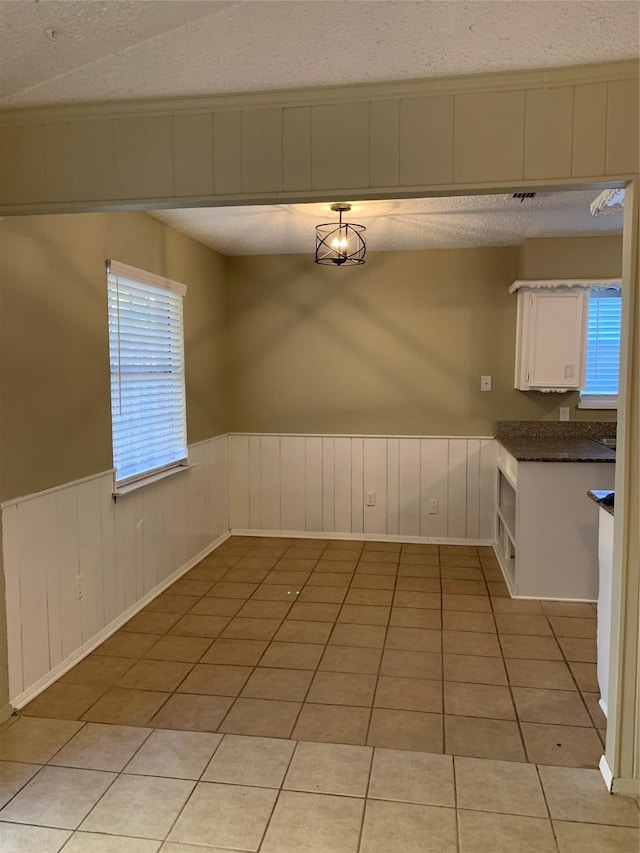 5410 Kings Manor Dr, Lake Dallas, TX 75065 - unfurnished dining area featuring a textured ceiling, light tile patterned floors, and wainscoting