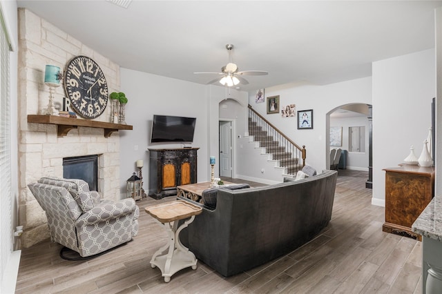 324 Roscoe Dr, Fate, TX 75087 - living room featuring arched walkways, a stone fireplace, a ceiling fan, wood finished floors, and stairway