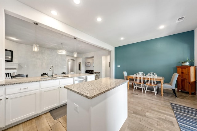705 Rio Concho Trl, Mckinney, TX 75071 - kitchen featuring stainless steel dishwasher, white cabinetry, a center island, light stone countertops, and light wood-style flooring