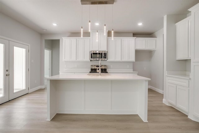 507 S 4th St, Grandview, TX 76050 - kitchen with stainless steel appliances, white cabinets, a kitchen island with sink, light wood finished floors, and light countertops