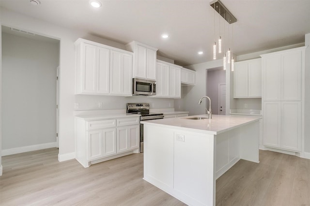 507 S 4th St, Grandview, TX 76050 - kitchen with appliances with stainless steel finishes, light wood-type flooring, a kitchen island with sink, white cabinetry, and light countertops