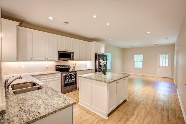 109 W Damon St, Terrell, TX 75160 - kitchen featuring appliances with stainless steel finishes, a center island, backsplash, light wood finished floors, and white cabinetry
