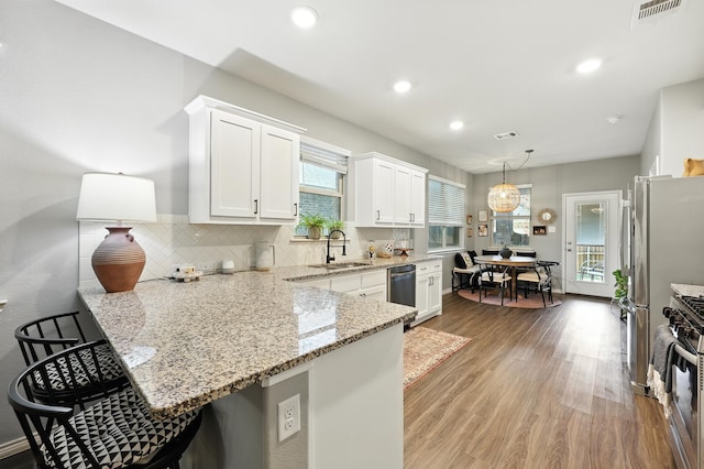 2136 Miramar Dr, Little Elm, TX 75068 - kitchen with stainless steel appliances, a peninsula, white cabinetry, a kitchen breakfast bar, and wood finished floors