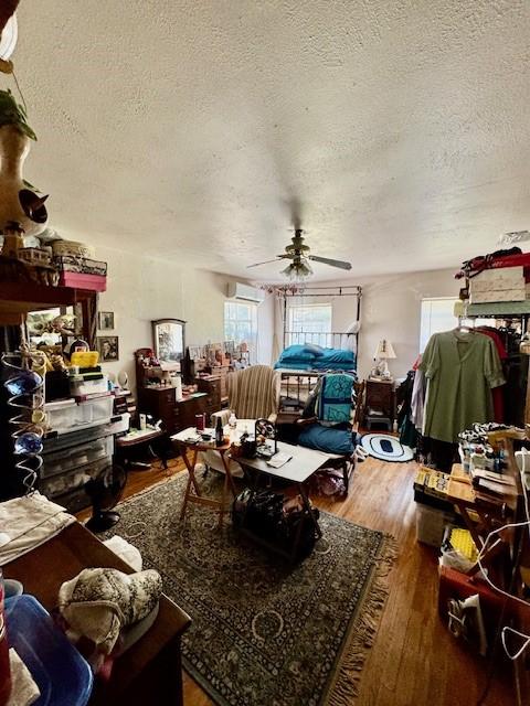 2025 16th St, Garland, TX 75041 - living area with plenty of natural light, a textured ceiling, a wall mounted air conditioner, a ceiling fan, and wood finished floors