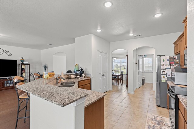 104 Knoll Ln, Decatur, TX 76234 - kitchen with black range with electric stovetop, arched walkways, a kitchen bar, white microwave, and brown cabinetry