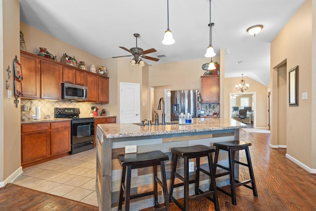 2912 Day Star Dr, Little Elm, TX 75068 - kitchen with stainless steel appliances, tasteful backsplash, a kitchen breakfast bar, a kitchen island with sink, and brown cabinetry