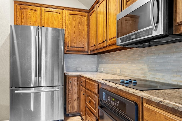12313 Ark Rd, Frisco, TX 75035 - kitchen with black appliances, tasteful backsplash, brown cabinets, light stone countertops, and lofted ceiling