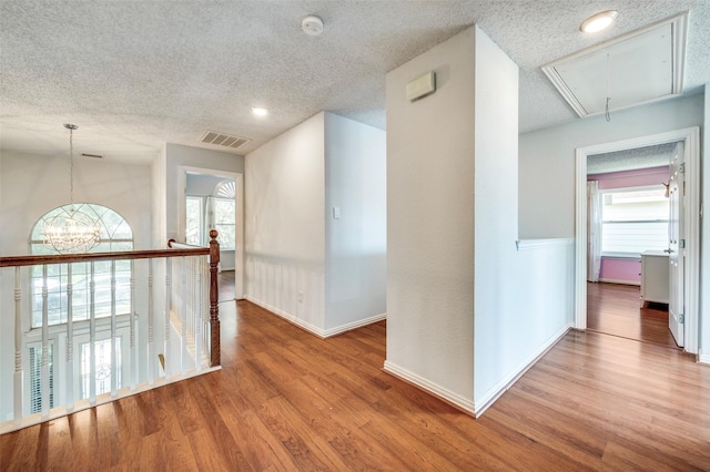 8224 Spring Valley Ln, Plano, TX 75025 - hall with attic access, wood finished floors, plenty of natural light, a textured ceiling, and a chandelier