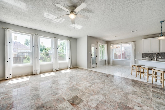 8224 Spring Valley Ln, Plano, TX 75025 - unfurnished living room with plenty of natural light, a ceiling fan, a textured ceiling, and a chandelier