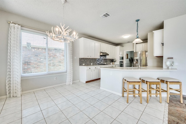 8224 Spring Valley Ln, Plano, TX 75025 - kitchen featuring under cabinet range hood, a chandelier, healthy amount of natural light, a peninsula, and a textured ceiling