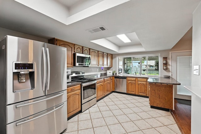 4201 Blackwillow Dr, Mesquite, TX 75150 - kitchen with stainless steel appliances, a raised ceiling, brown cabinets, dark countertops, and a peninsula