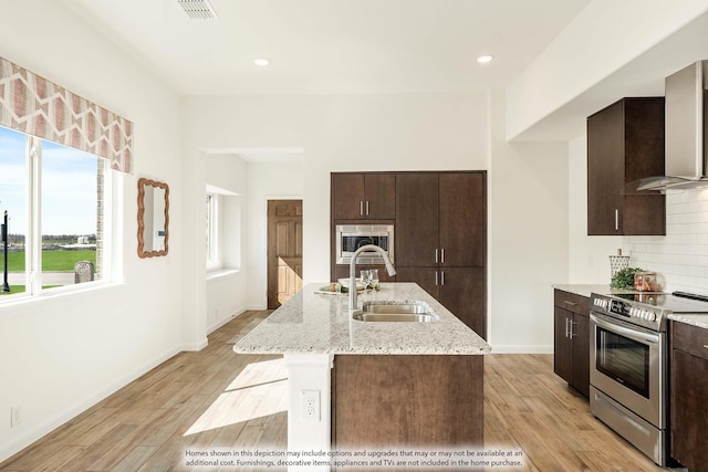 155 Wild Oak Gln, Lavon, TX 75166 - kitchen featuring appliances with stainless steel finishes, wall chimney range hood, dark brown cabinetry, light wood-style flooring, and backsplash