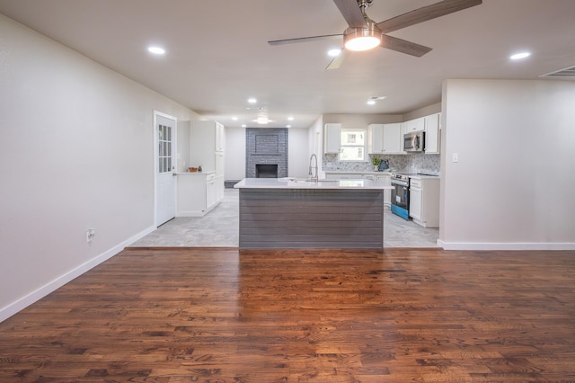 820 Vickie Dr, Azle, TX 76020 - kitchen with appliances with stainless steel finishes, a fireplace, ceiling fan, a center island with sink, and light countertops