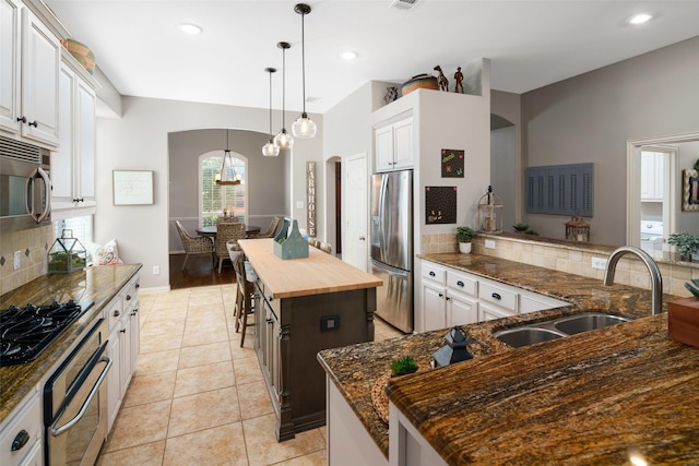 7716 Glenwood Springs Ln, Mckinney, TX 75070 - kitchen with stainless steel appliances, arched walkways, backsplash, wooden counters, and a center island