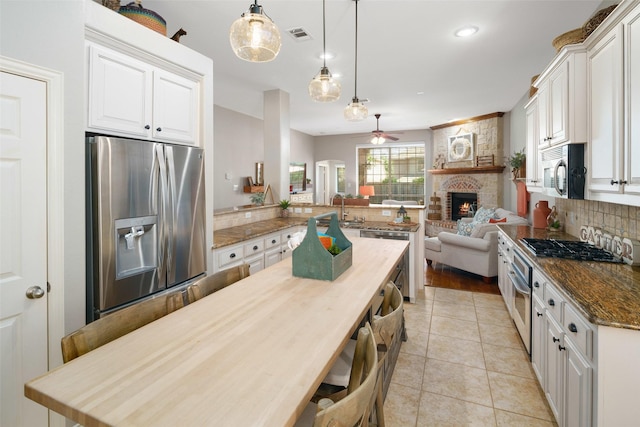 7716 Glenwood Springs Ln, Mckinney, TX 75070 - kitchen featuring appliances with stainless steel finishes, ceiling fan, open floor plan, backsplash, and a fireplace