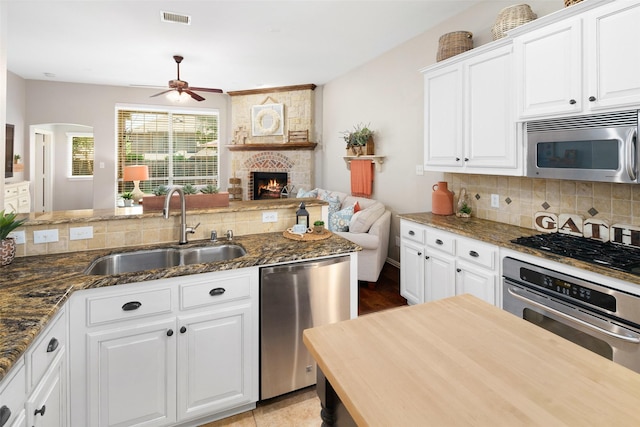 7716 Glenwood Springs Ln, Mckinney, TX 75070 - kitchen featuring appliances with stainless steel finishes, a ceiling fan, open floor plan, backsplash, and dark stone countertops