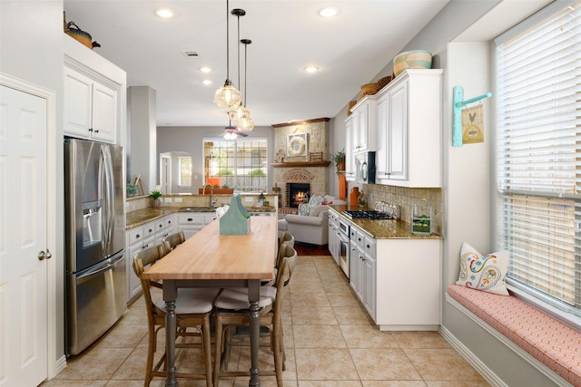 7716 Glenwood Springs Ln, Mckinney, TX 75070 - kitchen with appliances with stainless steel finishes, a fireplace, open floor plan, white cabinets, and tasteful backsplash