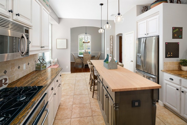 7716 Glenwood Springs Ln, Mckinney, TX 75070 - kitchen featuring butcher block counters, stainless steel appliances, arched walkways, decorative backsplash, and a center island