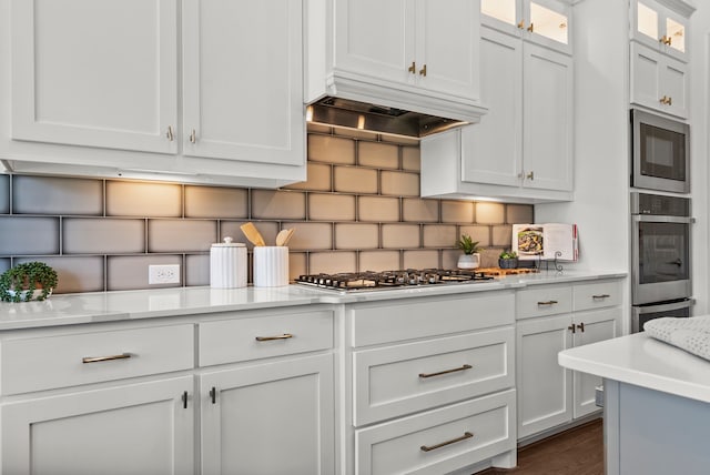 8133 Blumelia Dr, Dallas, TX 75252 - kitchen featuring appliances with stainless steel finishes, light countertops, white cabinetry, tasteful backsplash, and glass insert cabinets