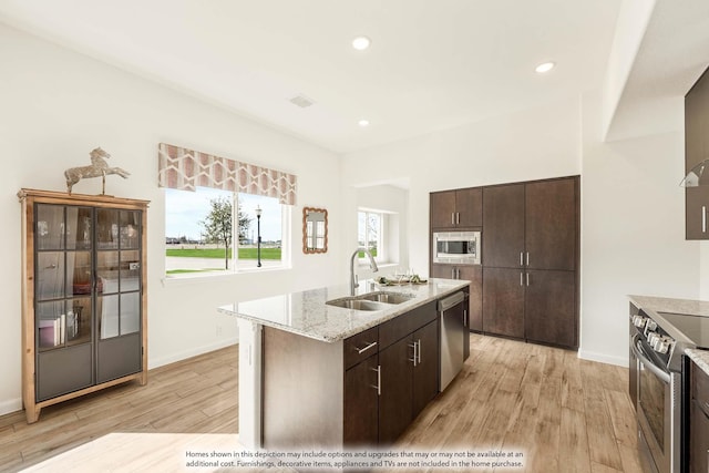 111 Cedar Grove Ct, Lavon, TX 75166 - kitchen with appliances with stainless steel finishes, light wood-type flooring, dark brown cabinets, a kitchen island with sink, and light stone countertops