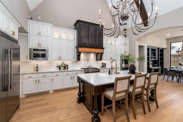 3208 Twin Eagles Dr, Celina, TX 75009 - kitchen featuring appliances with stainless steel finishes, arched walkways, a chandelier, high vaulted ceiling, and light wood finished floors